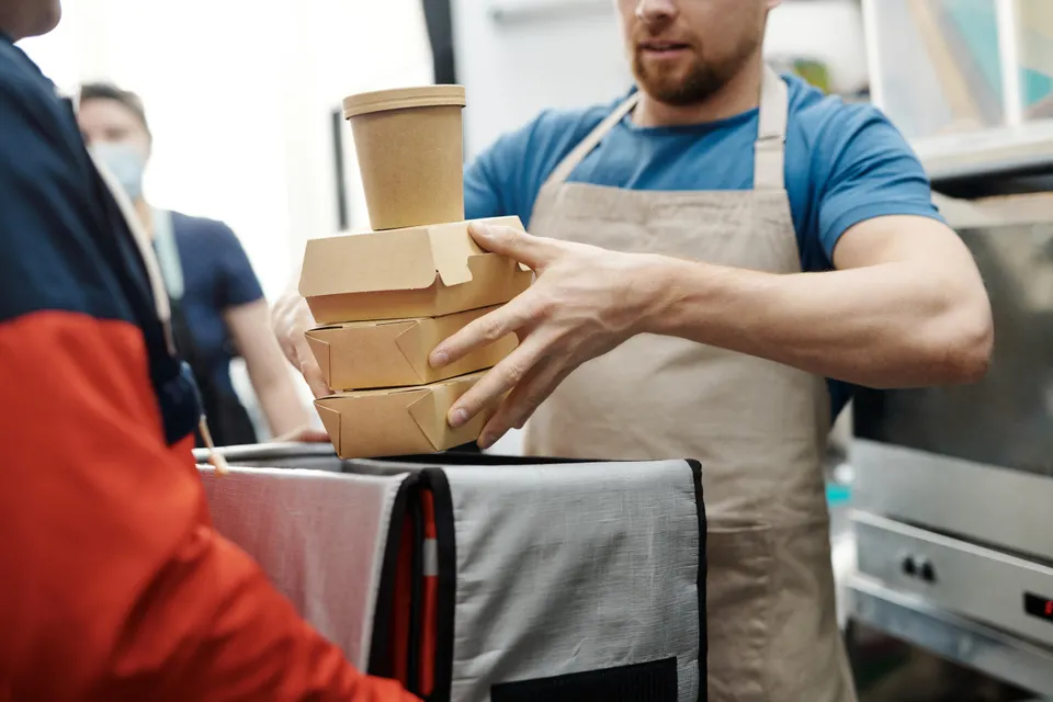Aşçı paket servis kutularını kuryenin çantasına veriyor
